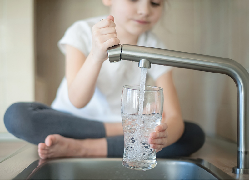 Kind zapft strukturiertes Trinkwasser am Wasserhahn in ein Glas